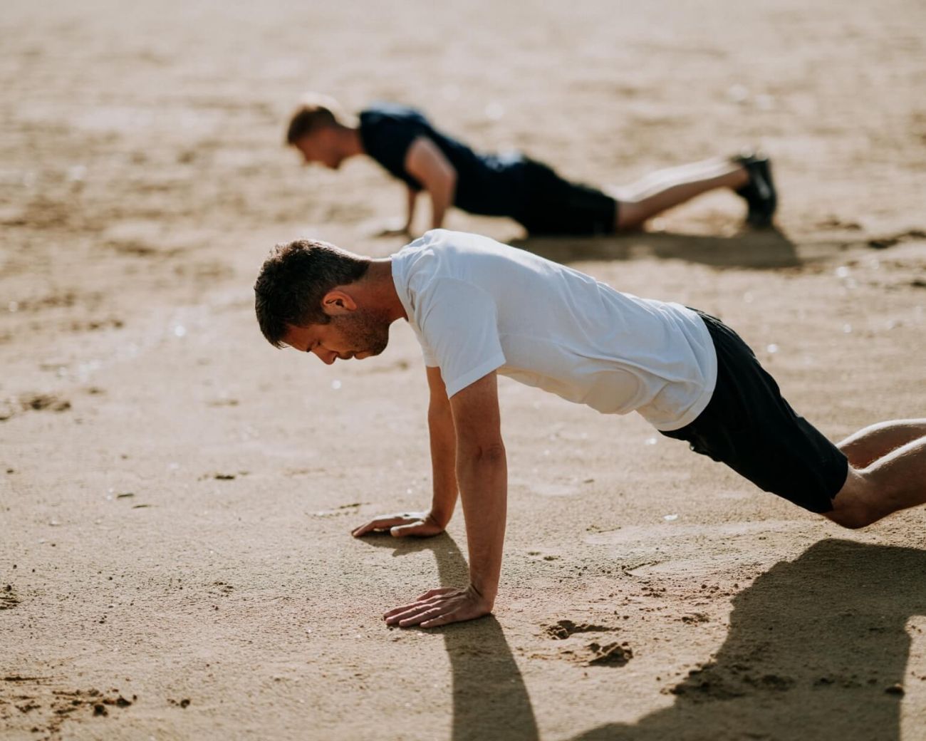 Fotografía de dos hombres realizando pushups en la playa