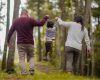 Fotografía de unos papas alzando a su hijo, cada uno de un brazo por el bosque
